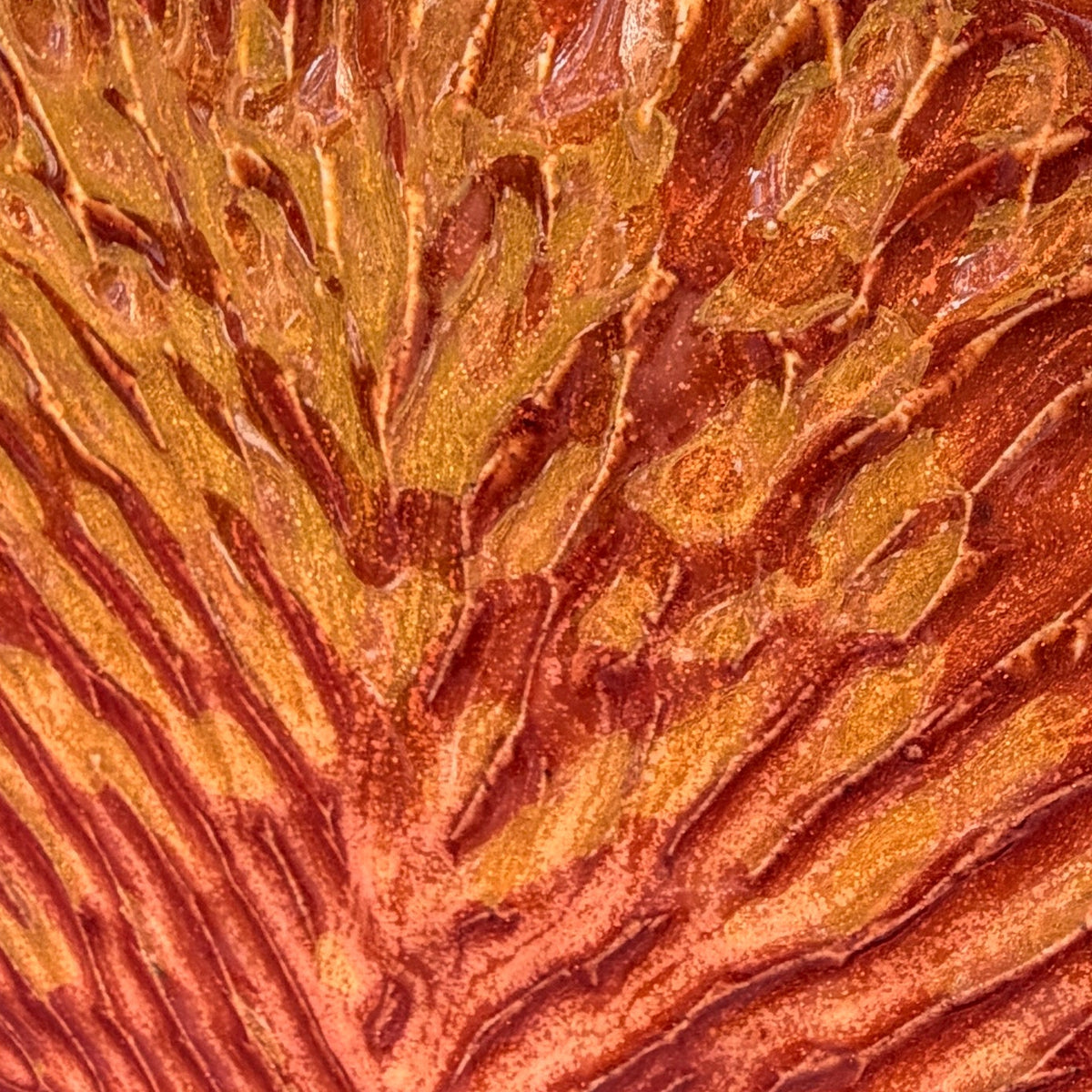 A small, fan-shaped ceramic plate or coaster with a textured, leaf-like pattern in orange and brown glaze, resting on a pink surface outdoors with a stone wall and trees in the background.