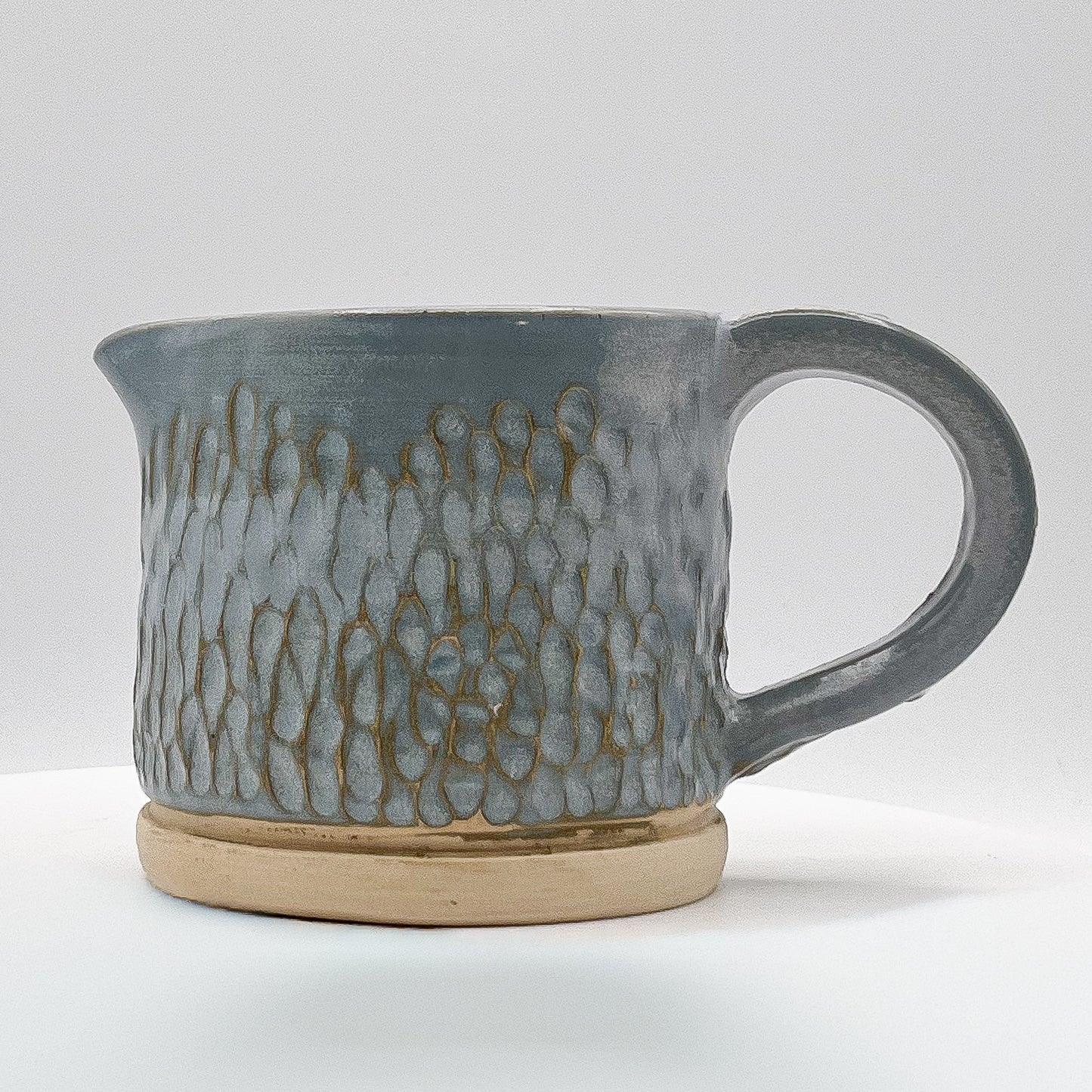 Gray ceramic pitcher with textured surface on a white background