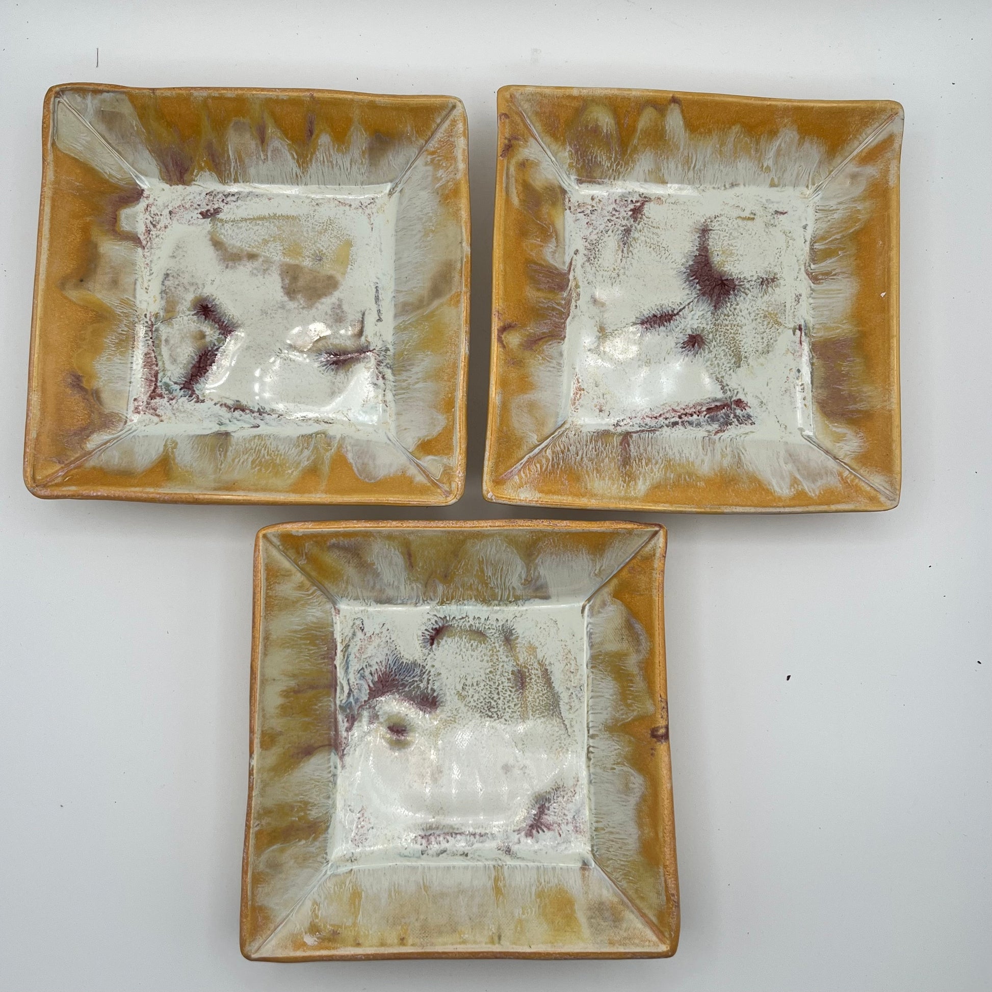 Three square ceramic plates with yellow and white design on a white background