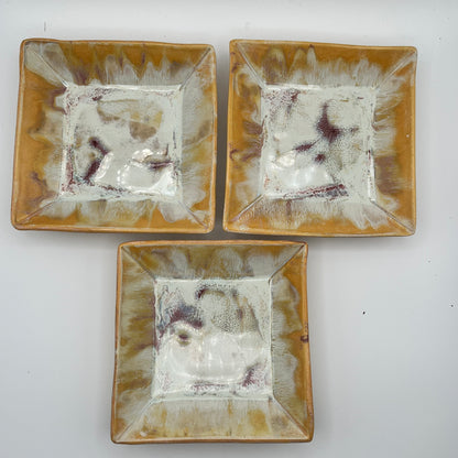 Three square ceramic plates with yellow and white design on a white background
