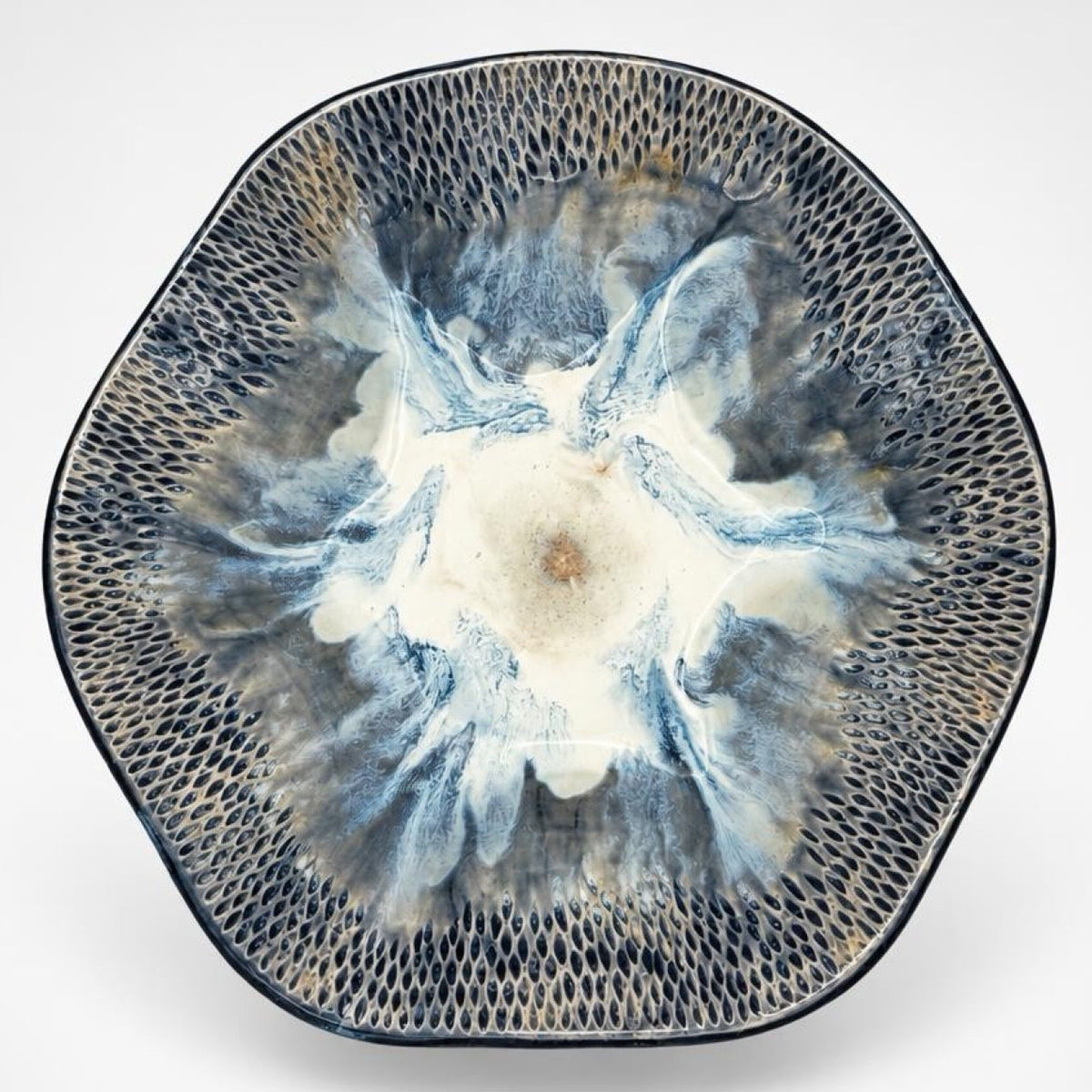 A round ceramic plate with a textured, honeycomb-like pattern around the rim and a central floral or watercolor burst in shades of blue, gray, and cream, set against a plain light gray background.