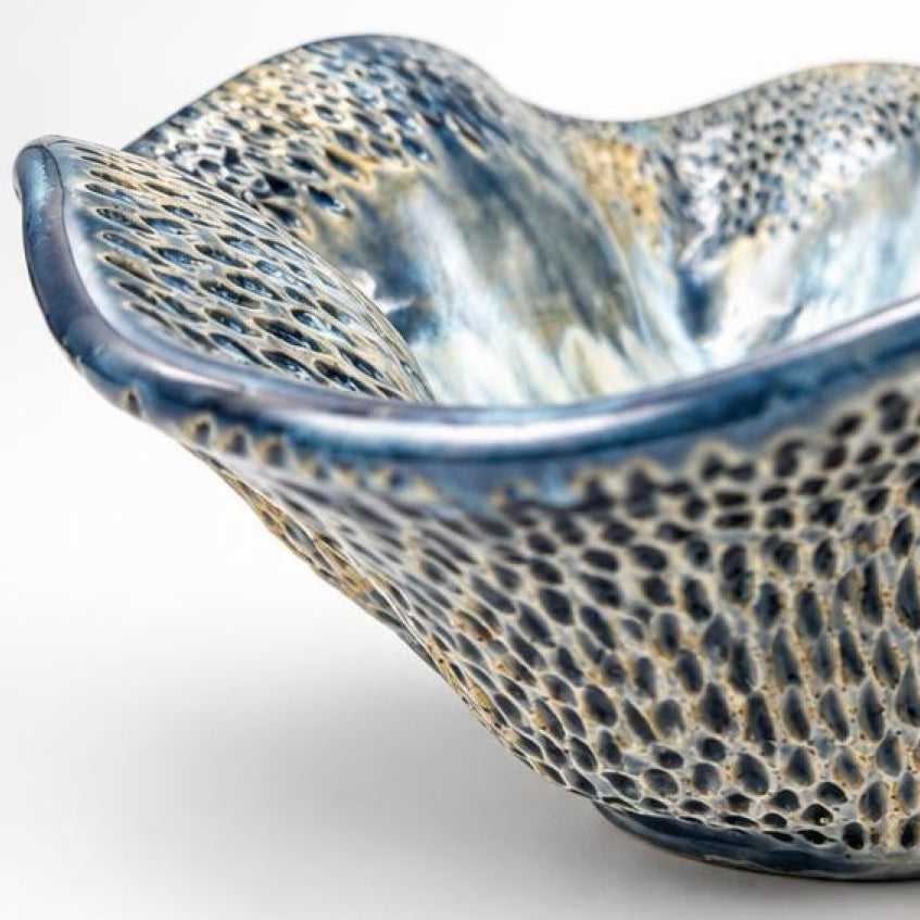 A handmade ceramic bowl with a wavy, scalloped rim and a textured, honeycomb-like pattern. The exterior features a speckled blue, black, and gold glaze, while the interior has a smooth, iridescent blue and white finish, set against a clean white background.