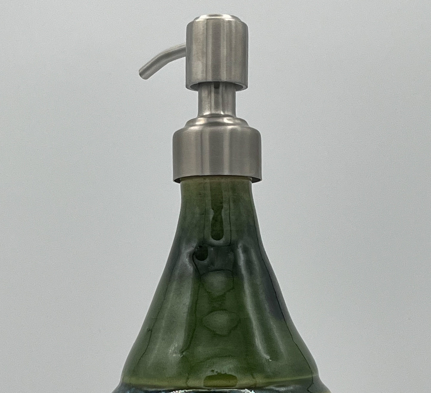 Green soap dispenser with a metallic pump on a gray background