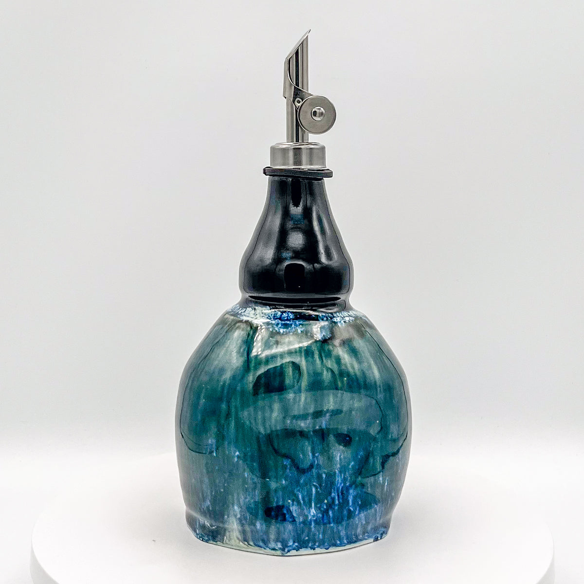 Ceramic oil bottle with blue marbled design and metal cap on a white background