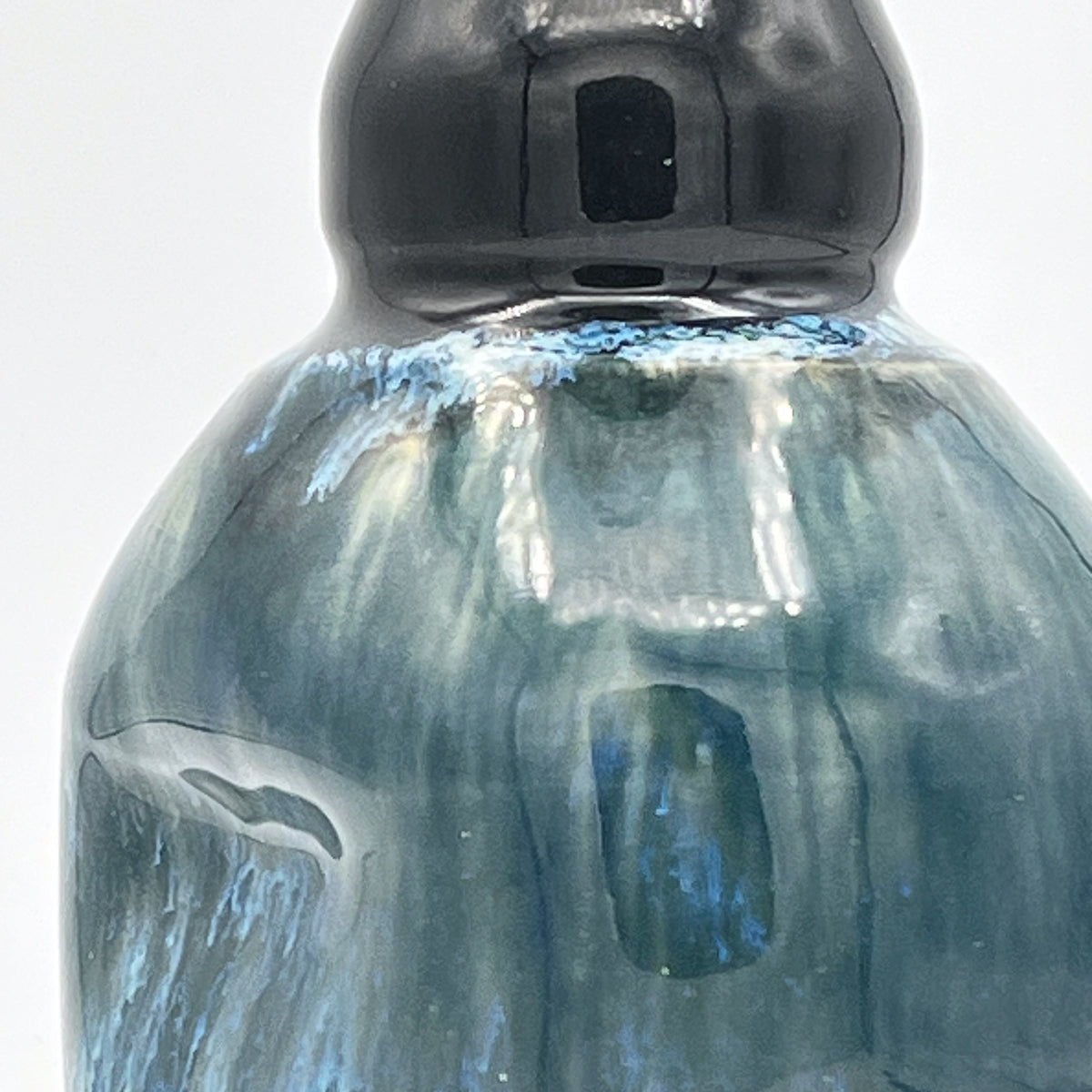 Close-up of a ceramic oil decanter with a black cap on a light gray background