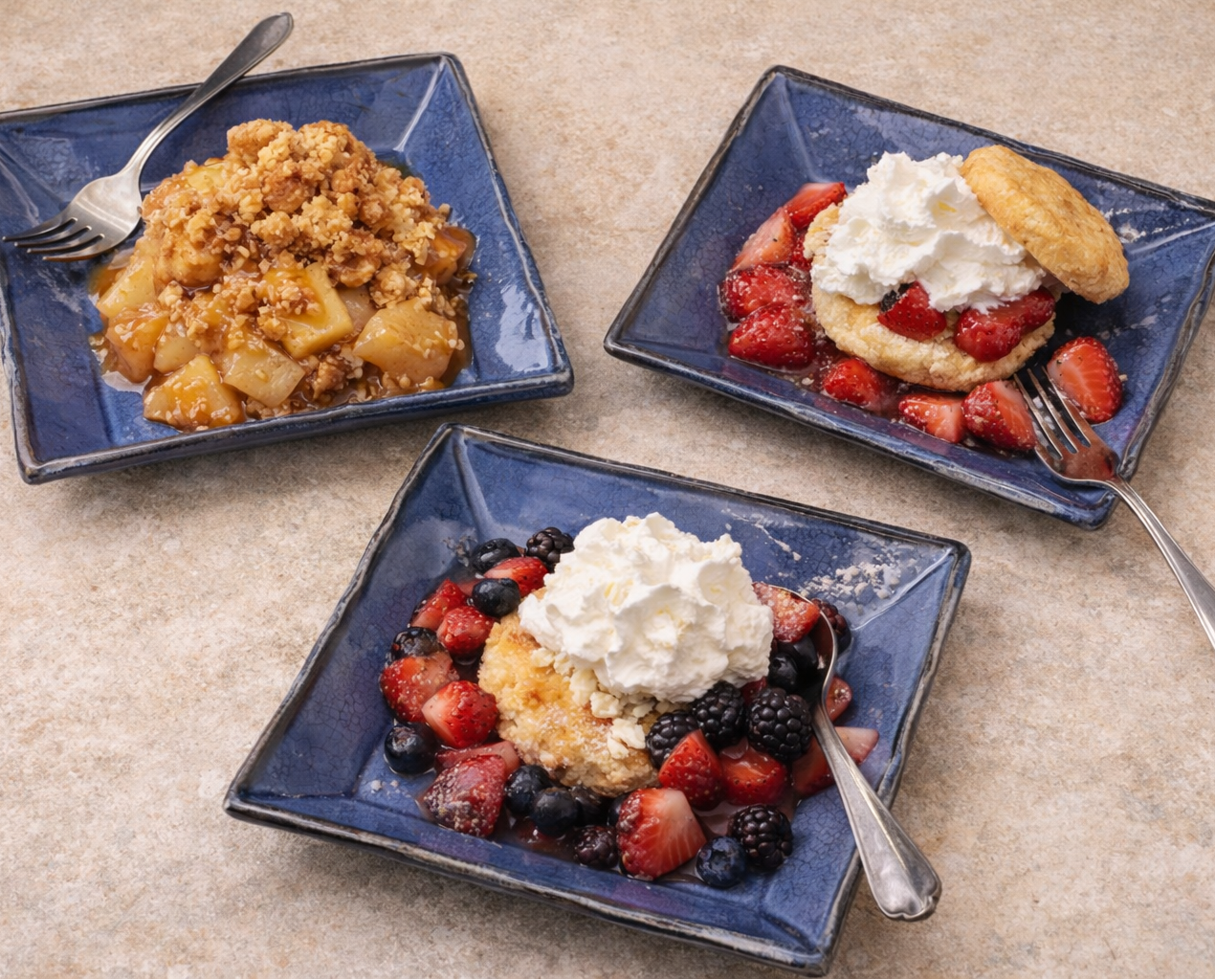 Three square blue plates with desserts on a beige surface
