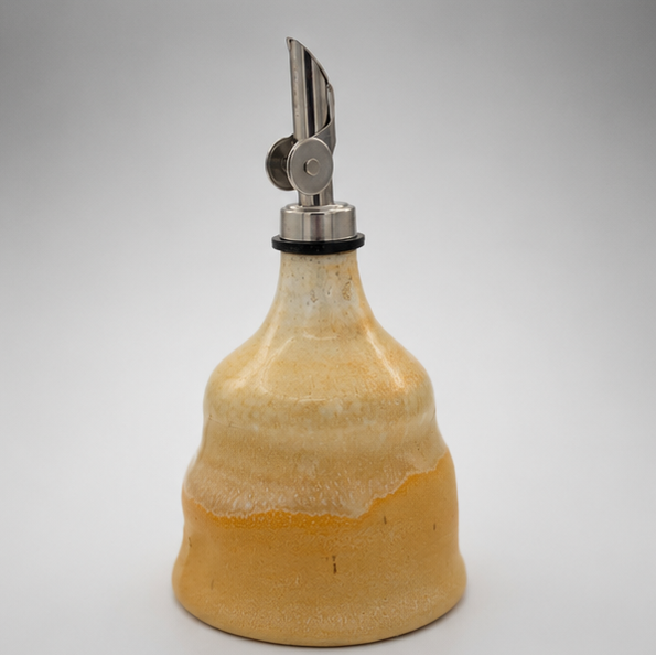 ceramic oil dispenser bottle with a flared yellow-orange glazed body, a silver metal pour spout, and a black rubber gasket, shown on a light gray background.