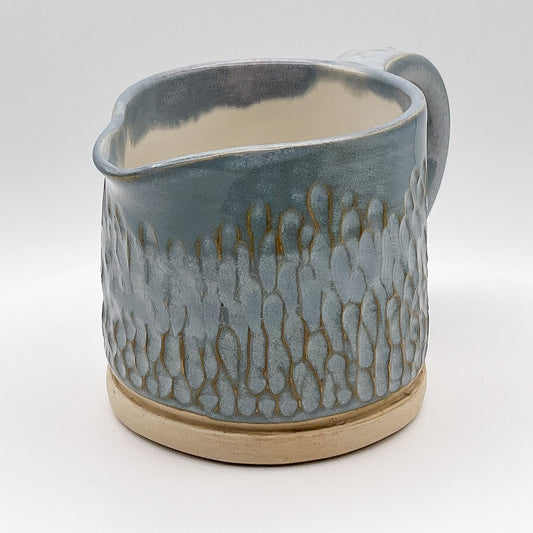 Ceramic pitcher with textured design on a white background