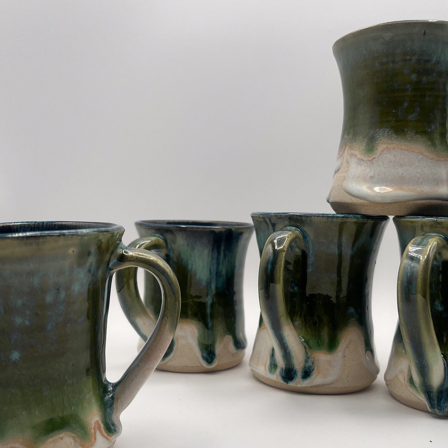 Set of five ceramic mugs with green and brown glaze on a white surface.
