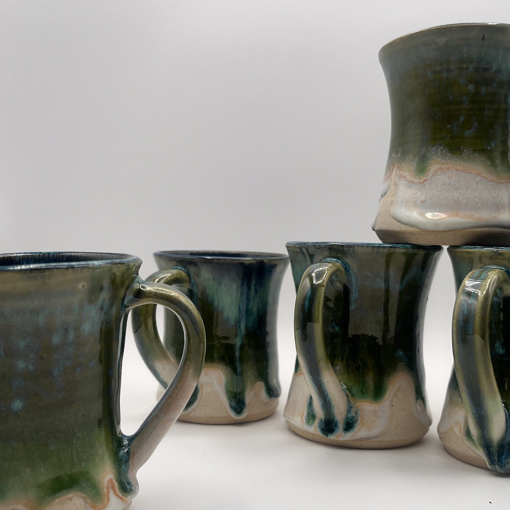 Set of five ceramic mugs with green and brown glaze on a white surface.