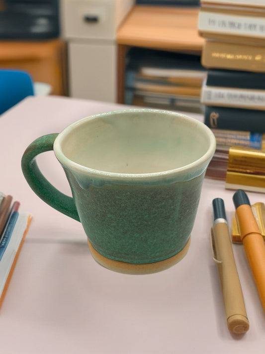 Green mug on a desk with books and pens in the background on the site Louise Moreau Studio